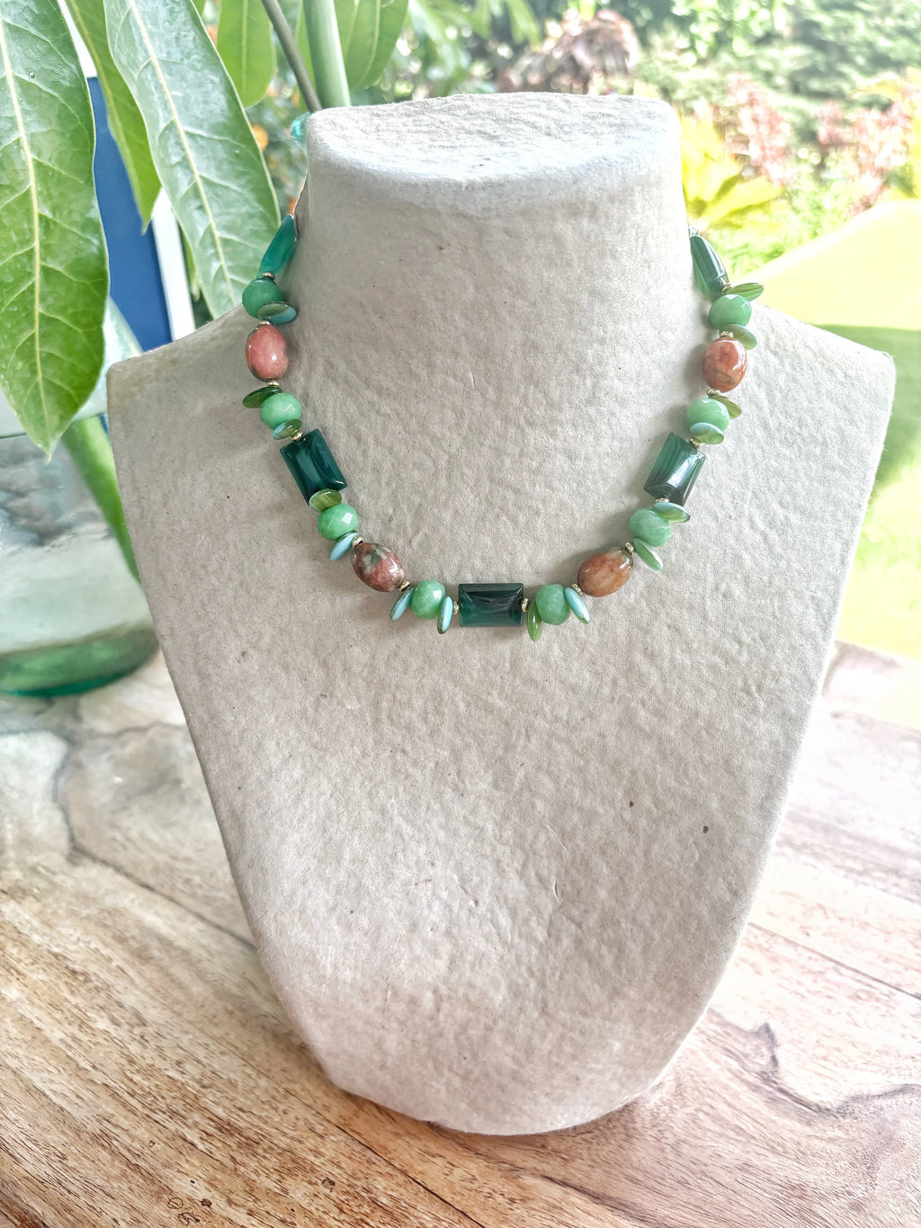 Collar corto artesanal de piedras semipreciosas verdes y rosadas con detalles metálicos, exhibido en busto de tela,.